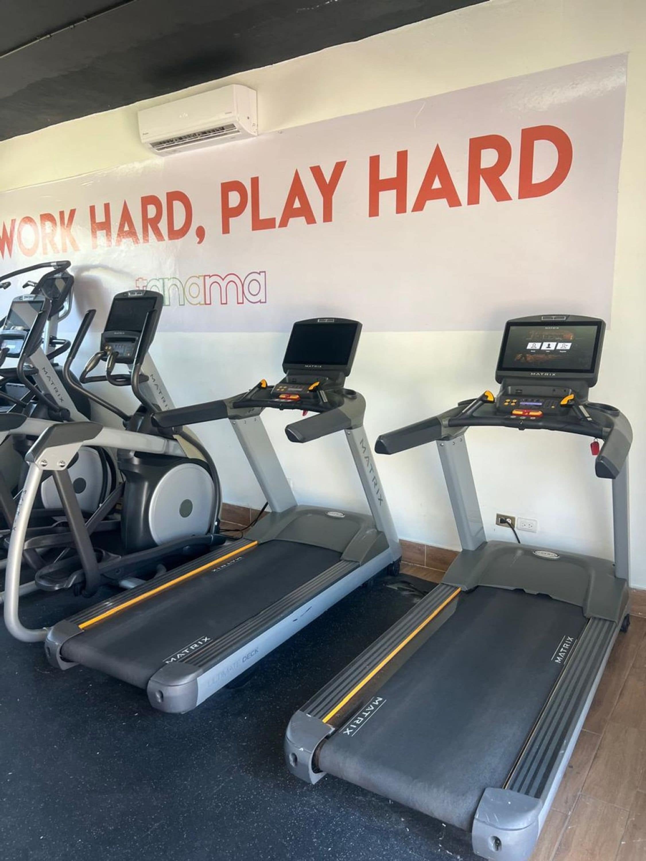 Tre tapis roulant in una palestra, con un poster motivazionale sullo sfondo.