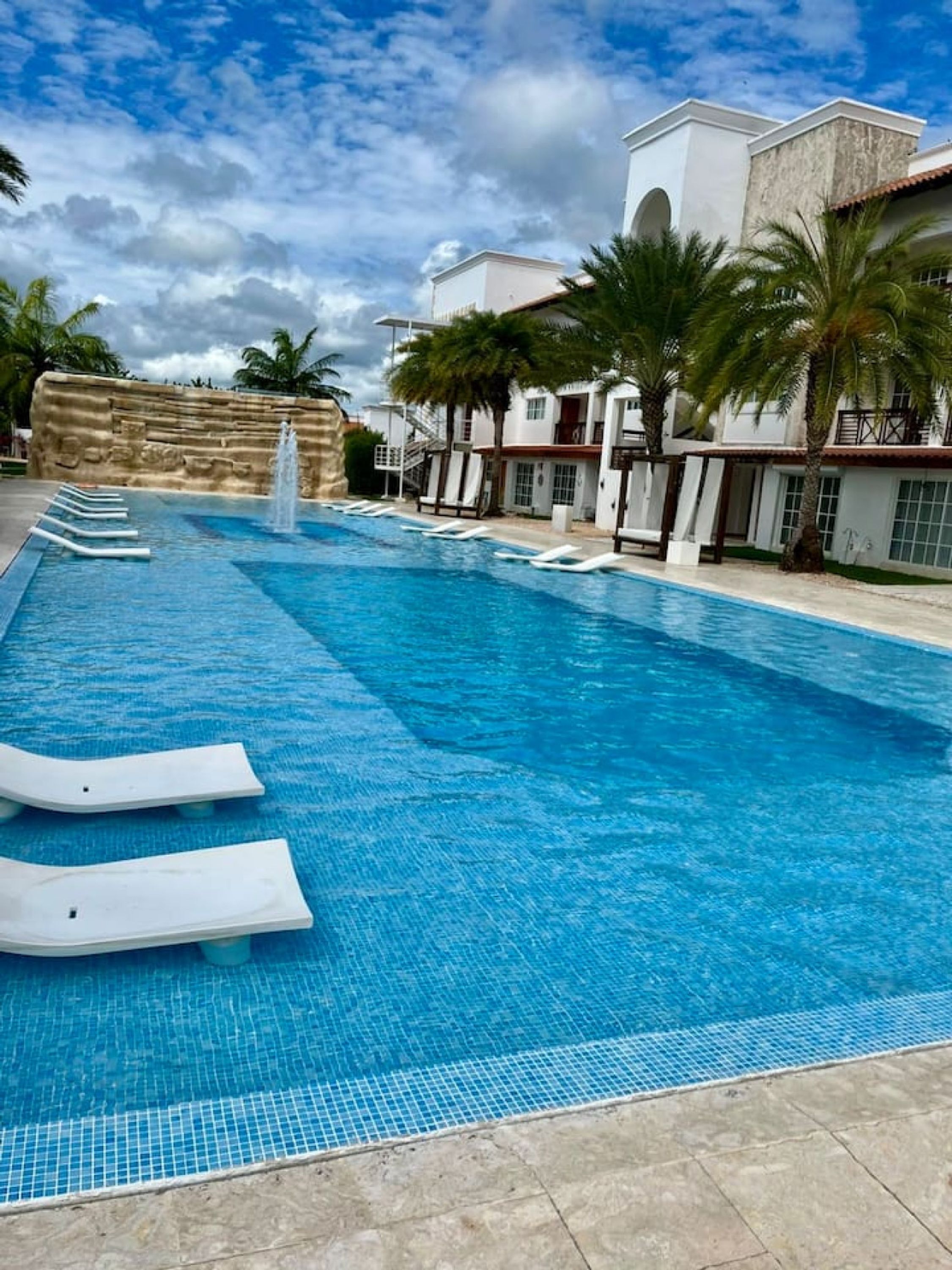 A swimming pool with clear blue water, a stone wall, and a building with a white facade and red roof.