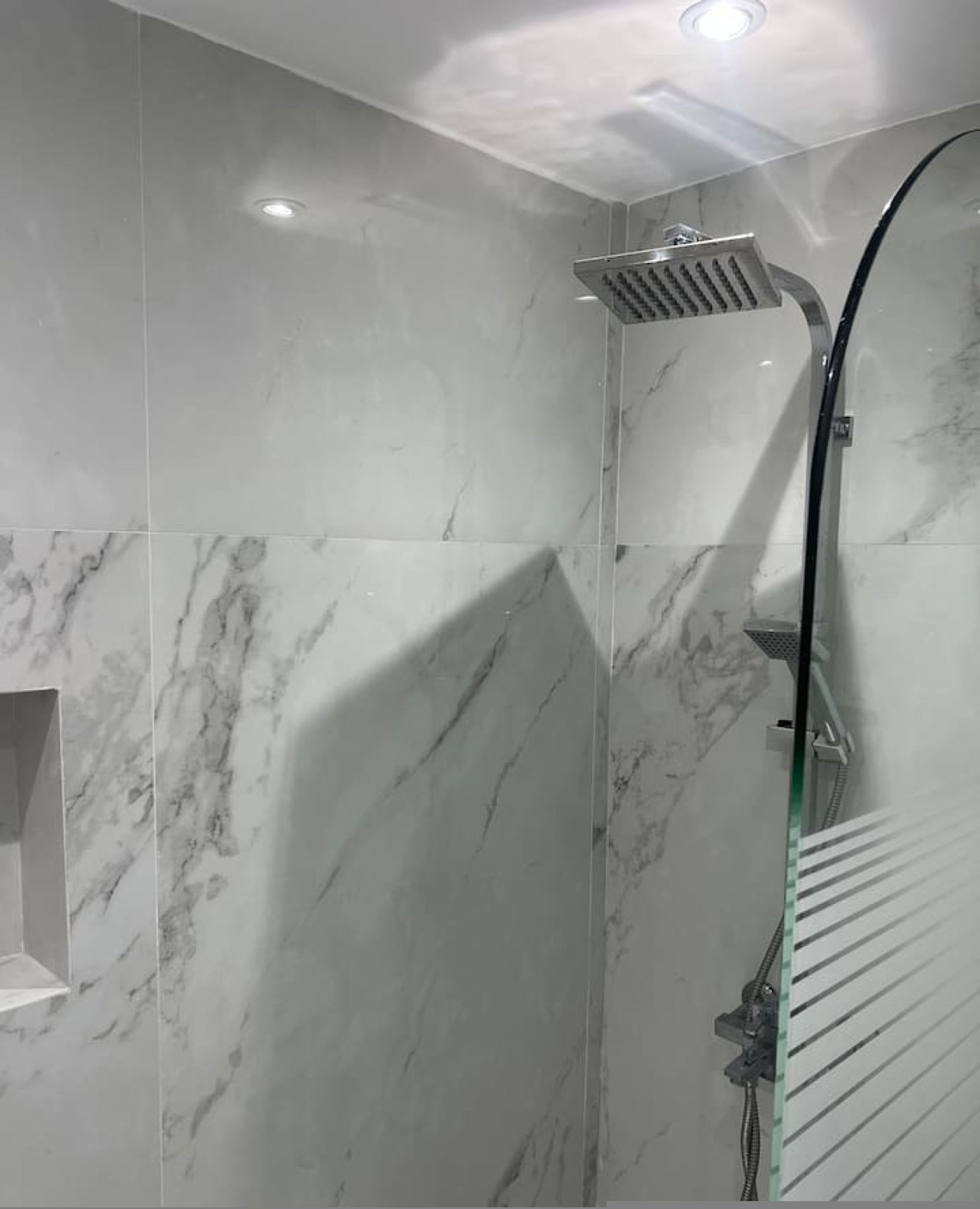 Une salle de bain moderne avec des murs en marbre, une douche en verre et un banc intégré.
