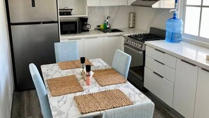 Une cuisine moderne avec des meubles blancs, un réfrigérateur en acier inoxydable, une cuisinière à gaz et un ventilateur de plafond.