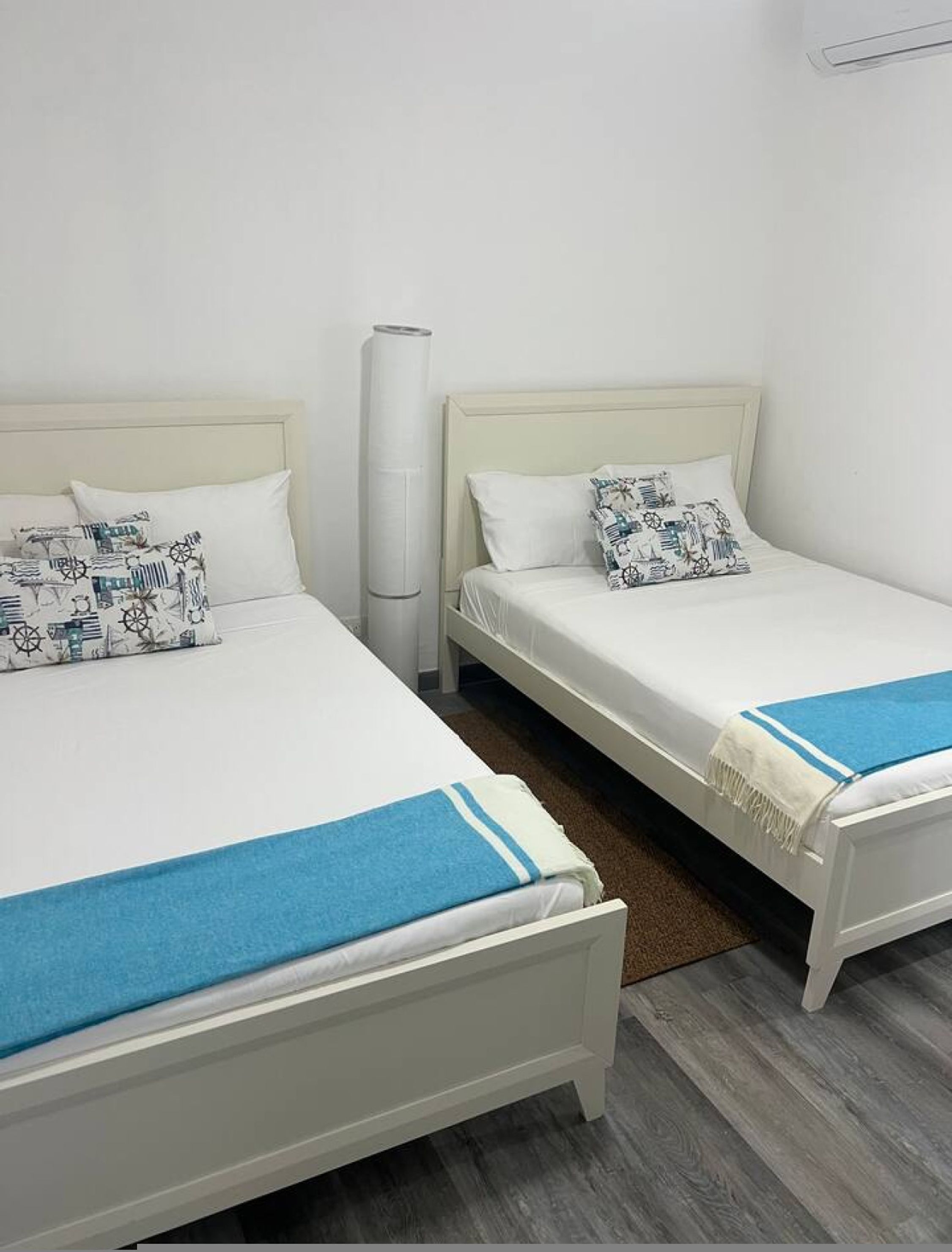 Two single beds with white headboards and matching pillows, a white bedside table, and a tall white air purifier between them.