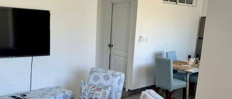 A living room with a sofa, two armchairs, a ceiling fan, a flat-screen TV, and a dining area with a table and chairs.