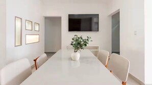 A modern conference room with a long table, white chairs, a large flat-screen TV, and framed pictures on the wall. - Private 3BR Villa Yard Pool Gated Sleeps 8 (La Romana)