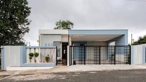 A modern building with a covered entrance, a gated driveway, and a landscaped area with small trees. - Private 3BR Villa Yard Pool Gated Sleeps 8 (La Romana)