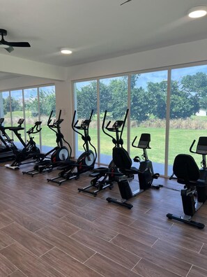 Ein Fitnessraum mit Ergometer, großen Fenstern und einem Deckenventilator.