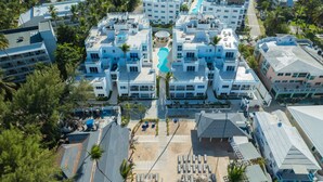 An aerial view of a resort with multiple buildings, a central pool, and a beach area with sun loungers. - Beachfront Condo 2 Pools Private Beach 8 Guest (Punta Cana)