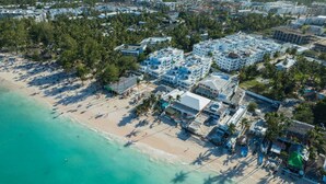 An aerial view of a coastal area with a beach, buildings, and palm trees. - Beachfront Condo 2 Pools Private Beach 8 Guest (Punta Cana)
