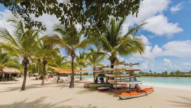 A beach with palm trees, a thatched-roof hut, and kayaks. - 2BR Love Nest Jacuzzi Gym 1 Free Excursion (Punta Cana)