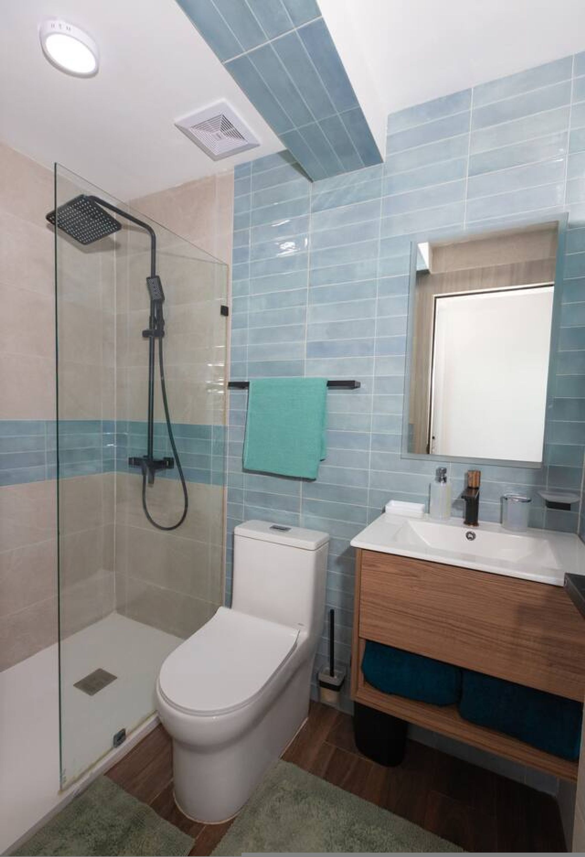 A bathroom with a glass-enclosed shower, a white toilet, a wooden vanity with a mirror, and blue-tiled walls.