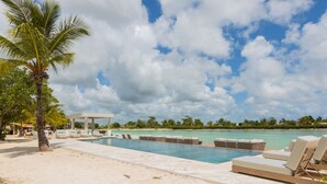 A poolside area with lounge chairs, a palm tree, and a building in the background. - 2BR Love Nest Jacuzzi Gym 1 Free Excursion (Punta Cana)