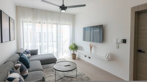 A modern living room with a sofa, a coffee table, a ceiling fan, a TV, and a potted plant. - 2BR Love Nest Jacuzzi Gym 1 Free Excursion (Punta Cana)