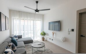 Ein modernes Wohnzimmer mit Sofa, Couchtisch, Deckenventilator, Fernseher und einer Topfpflanze.