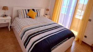 A bedroom with a bed, bedside tables, a hanging light fixture, and a window with curtains. - Beachfront 3BR Condo w Pool Views Sleeps 10 (San Javier)