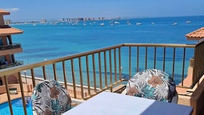 A balcony with a table and chairs, overlooking a pool and the sea with boats. - Beachfront 3BR Condo w Pool Views Sleeps 10 (San Javier)