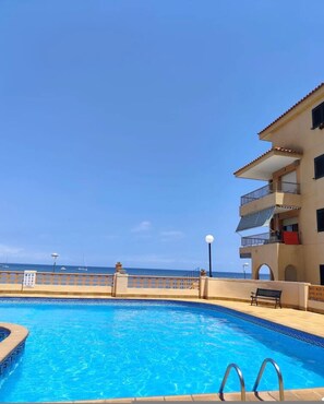 Une piscine offrant une vue dégagée sur l’océan, un bâtiment doté de balcons et un banc.