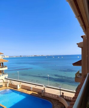 Une vue sur la piscine, avec une mer d’un bleu limpide, une jetée au loin et un balcon donnant sur l’eau.