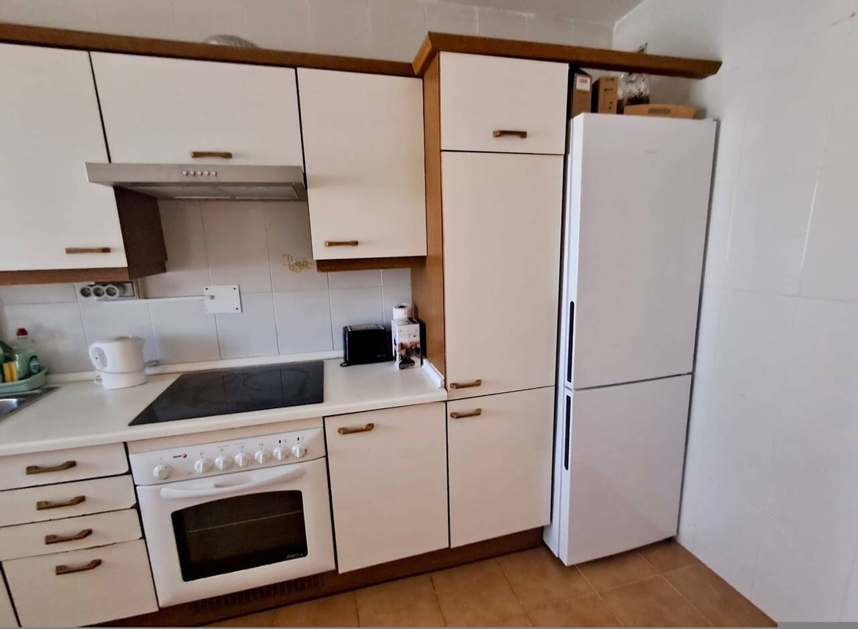 A kitchen with white cabinets, a stove, oven, microwave, and a refrigerator.