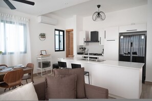 Una cocina moderna con armarios blancos, una isla central y una zona de comedor con sofá y sillas.