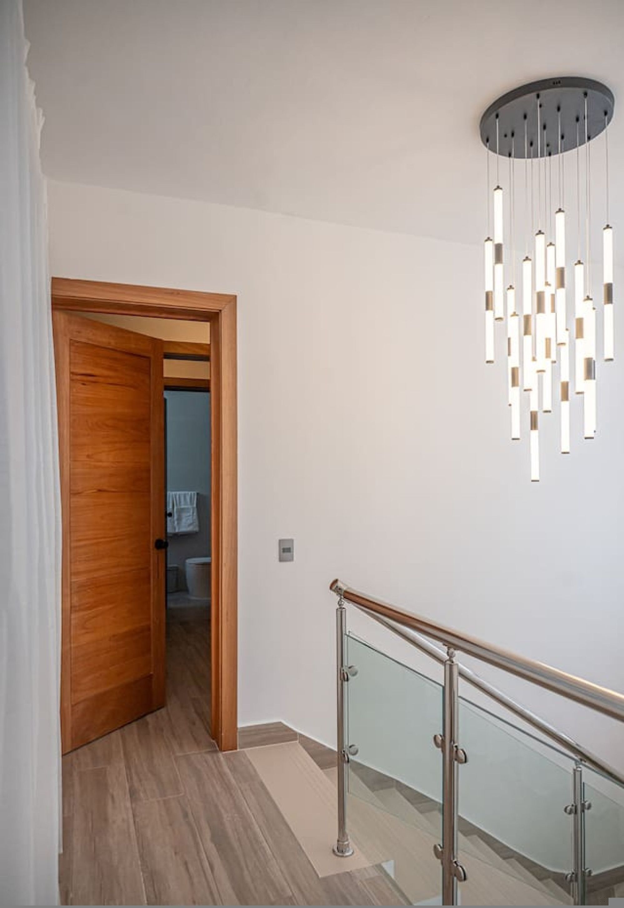Un interno moderno con una porta in legno, una scala con ringhiere in vetro e un lampadario.