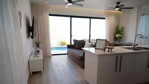 Una cocina moderna con una isla central, un área de comedor con sofá y un amplio ventanal corredero que da a una piscina.