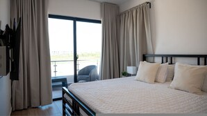 Un dormitorio con una cama grande, televisor y un balcón con cortinas.