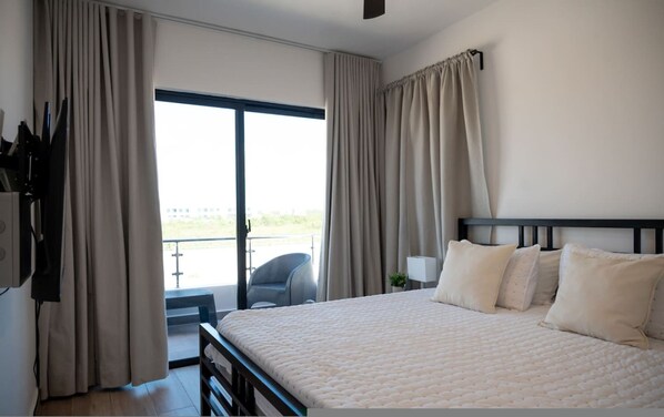 Un dormitorio con una cama grande, televisor y un balcón con cortinas.