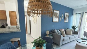 Un saló modern amb una paret blava, una taula de dinar de vidre i una làmpada penjant de vimet.
