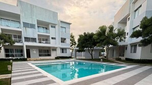 Un edifici modern amb piscina, passeres pavimentades i vegetació circumdant.