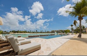 A poolside area with lounge chairs, a clear blue sky, and a beach in the background. - Rooftop Jacuzzi Condo Free Airport Transfer (Punta Cana)