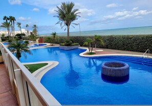 A swimming pool with a view of the sea, surrounded by palm trees and a hedge. - 2BR Ocean View Beach Apartment Pool La Manga (Cartagena)