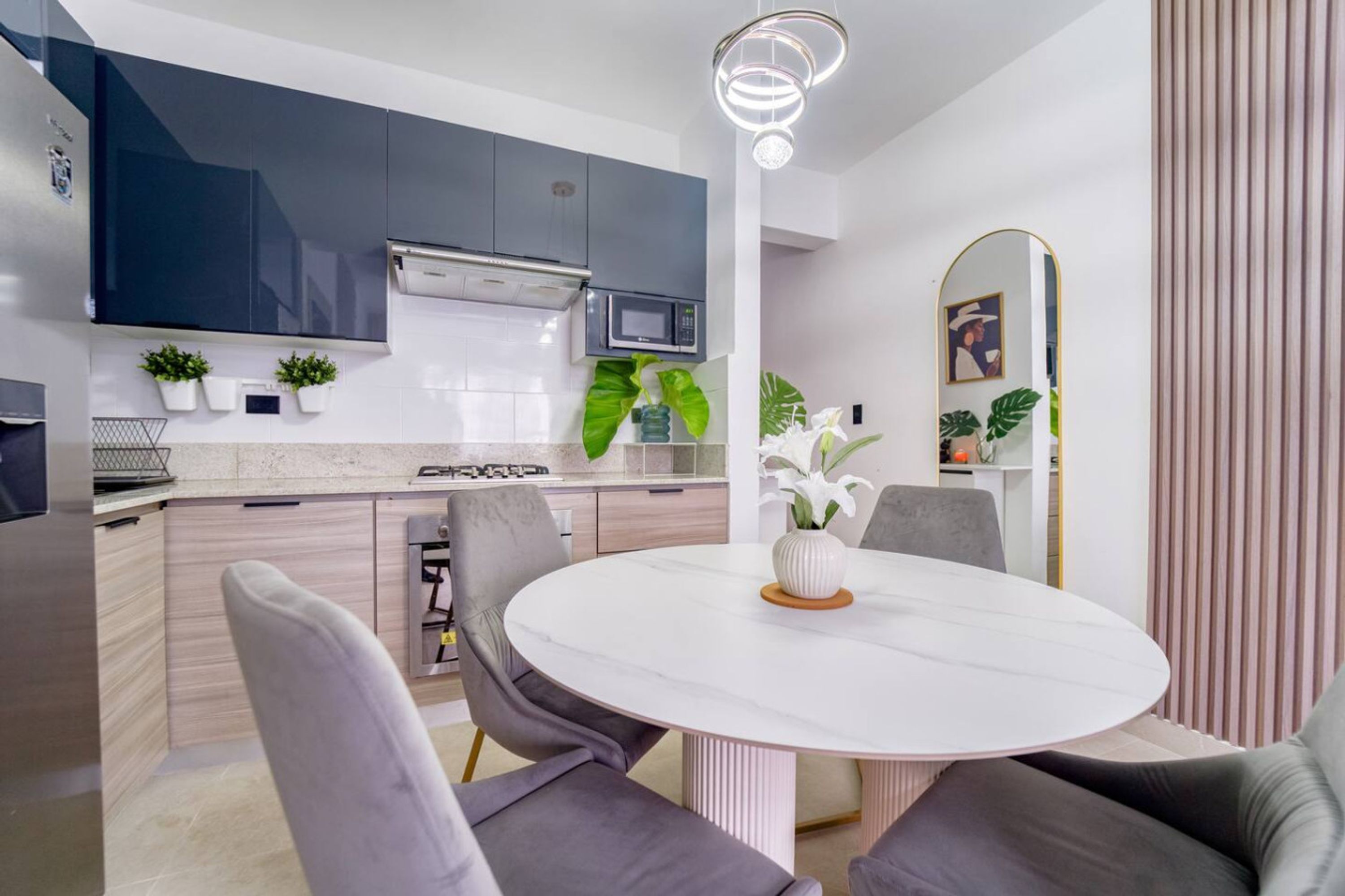 A modern kitchen with grey cabinets, a white countertop, and a round dining table with grey chairs.