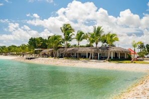 Ein Strandhotel mit strohgedeckten Gebäuden, Palmen und freiem Blick auf den Ozean.