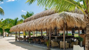 A beachside restaurant with thatched umbrellas, wicker furniture, and a view of the ocean. - 2-level Retreat Jacuzzi Free Airport Transfer (Punta Cana)