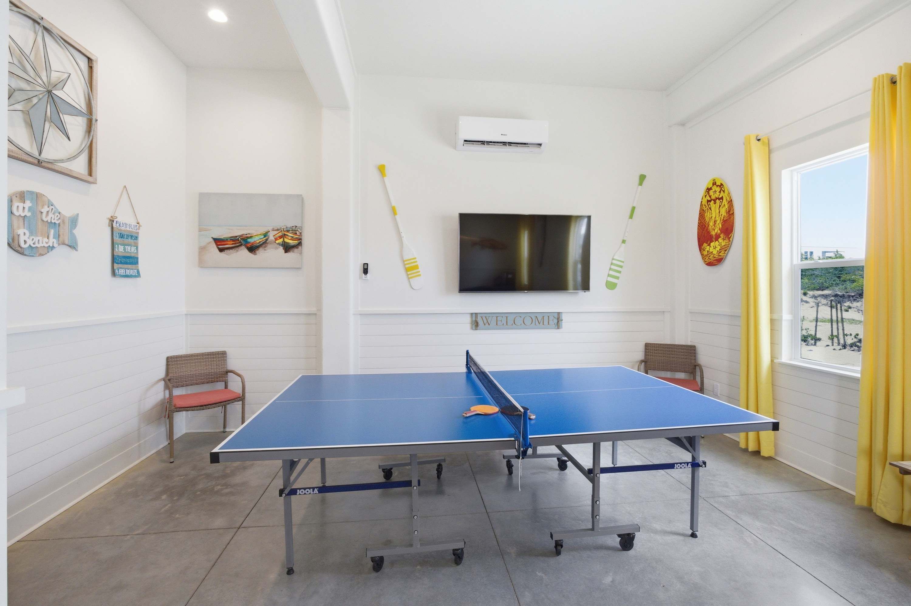 A ping pong table in a room with a TV, wall decorations, and a window with curtains.