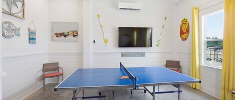 A ping pong table in a room with a TV, wall decorations, and a window with curtains.