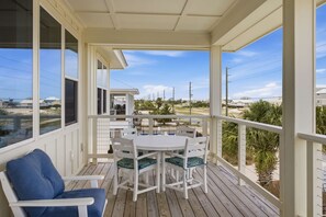 Ein überdachter Außenbereich mit Tisch und Stühlen, ein blauer Stuhl und Blick auf Strand und Häuser.