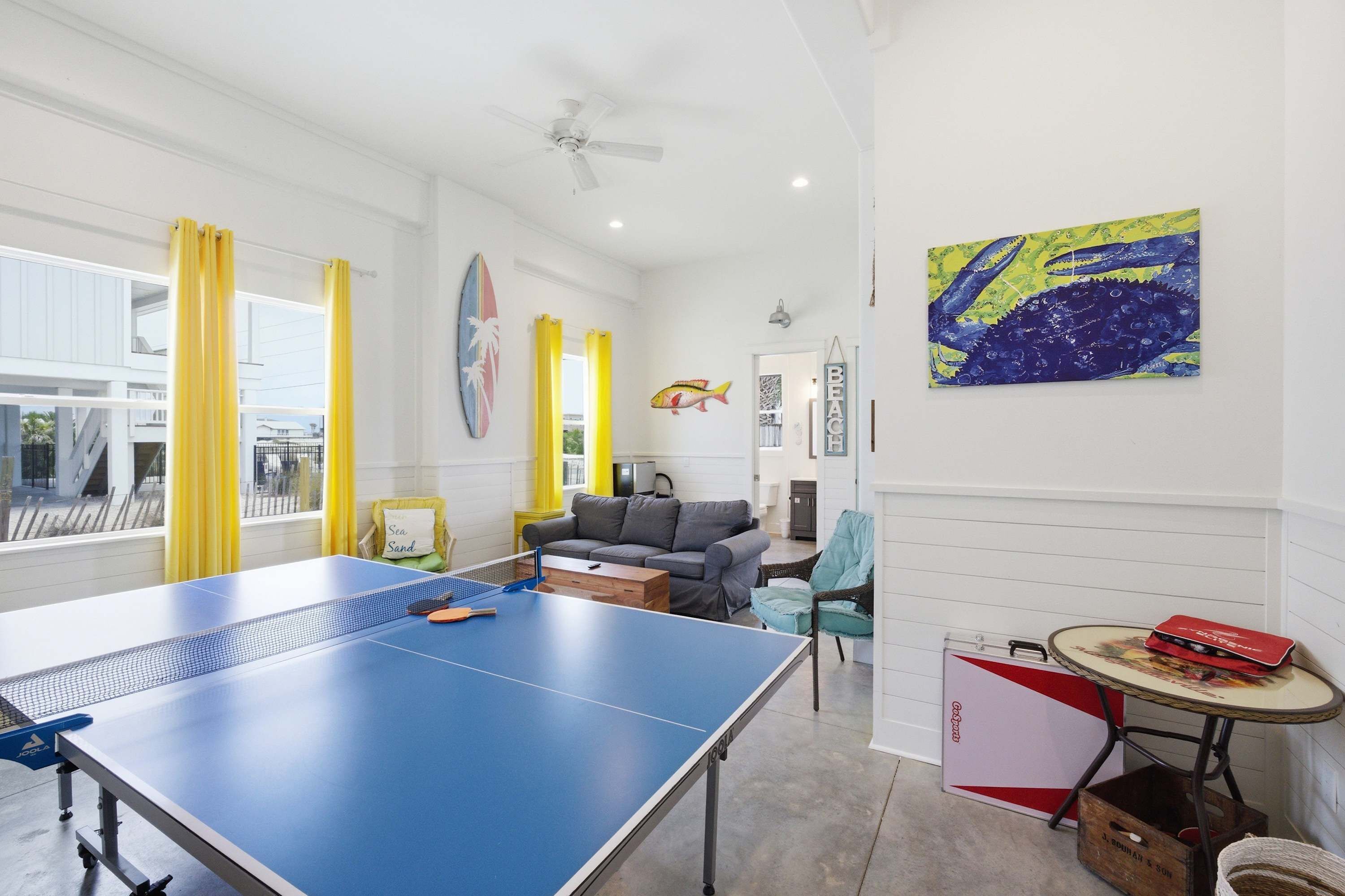 Une pièce avec une table de ping-pong, un canapé, une petite table sur laquelle se trouve un objet rouge, et un mur décoré avec un motif de poisson.