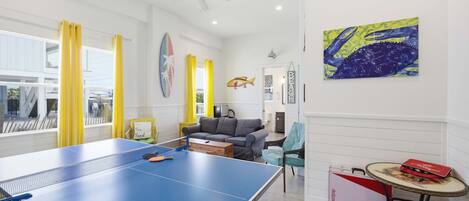 Une pièce avec une table de ping-pong, un canapé, une petite table sur laquelle se trouve un objet rouge, et un mur décoré avec un motif de poisson.
