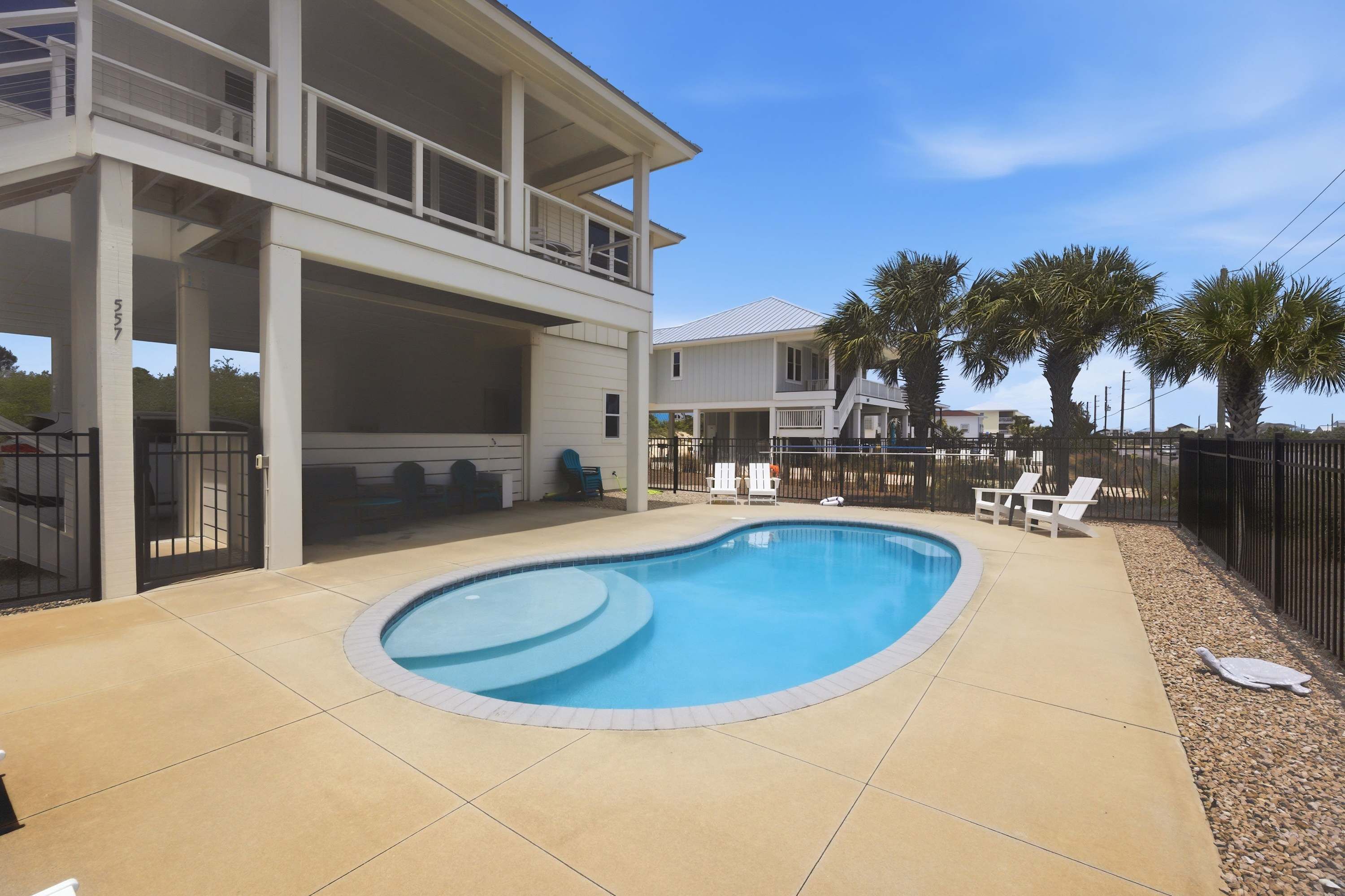 A two-story house with a swimming pool, outdoor seating, and palm trees.
