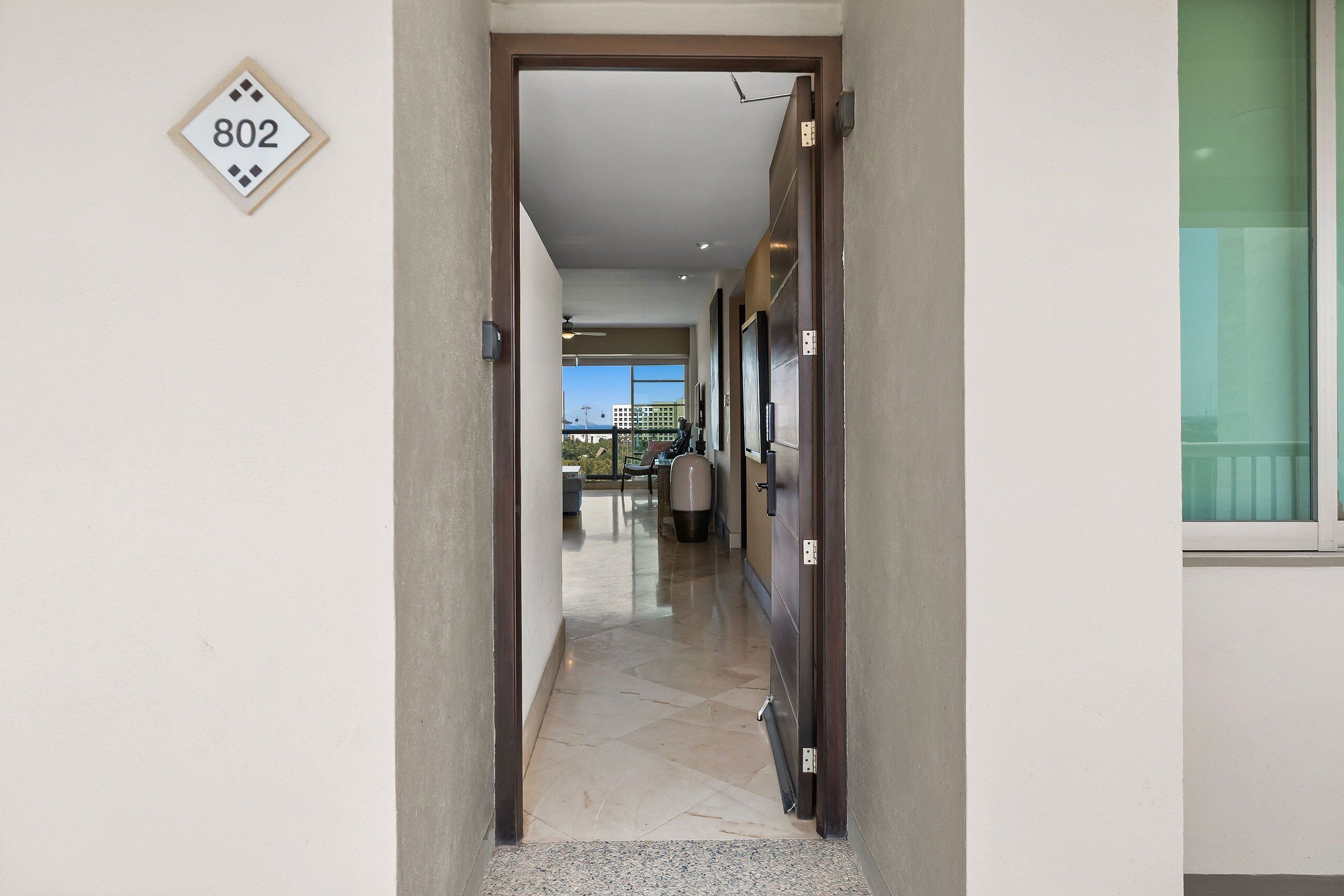 A hallway with a door marked '802' leading to a room with a view of a building and a balcony.