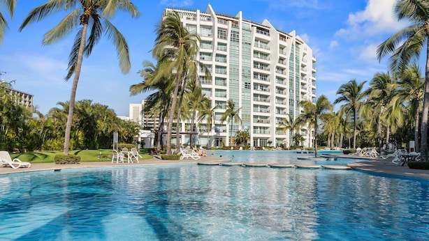 Un hotel con una grande piscina, palme e un edificio a più piani.