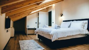 A bedroom with a wooden ceiling, a bed with white bedding, a bedside table, and a wall-mounted light fixture.