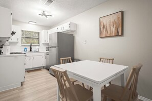 A modern kitchen with white cabinetry, a dining table with chairs, and a painting on the wall.