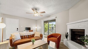 Un salon comprenant un canapé, un fauteuil, une table basse, une cheminée, un ventilateur de plafond et une porte.
