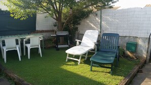 Een achtertuin met een groen gazon, een witte tafel en twee witte stoelen.