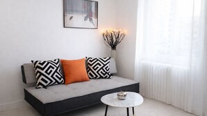Een moderne woonkamer met een grijze bank, gekleurde kussens, een klein rond tafeltje en een vaas met verlichting.