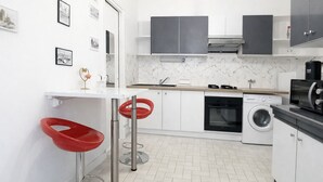 Een moderne keuken met een inbouwoven, magnetron en wasmachine, een witte marmeren spatwand en rode barkrukken.