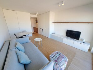 A modern living room with a sofa, a TV, a dining area, and a kitchen in the background. - Sea View Retreat for 2 in Oostduinkerke (Koksijde)