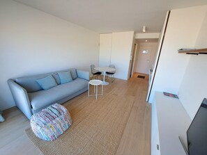 A modern living room with a grey sofa, a small round table, and a colorful pouf. - Sea View Retreat for 2 in Oostduinkerke (Koksijde)