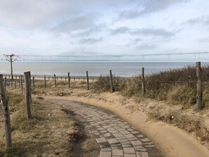 A paved pathway leading to a beach with a fence and vegetation. - Sea View Retreat for 2 in Oostduinkerke (Koksijde)